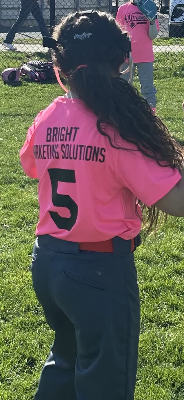 Player wearing a pink Bright Marketing Solutions sponsored jersey at a Dumont NJ youth softball game